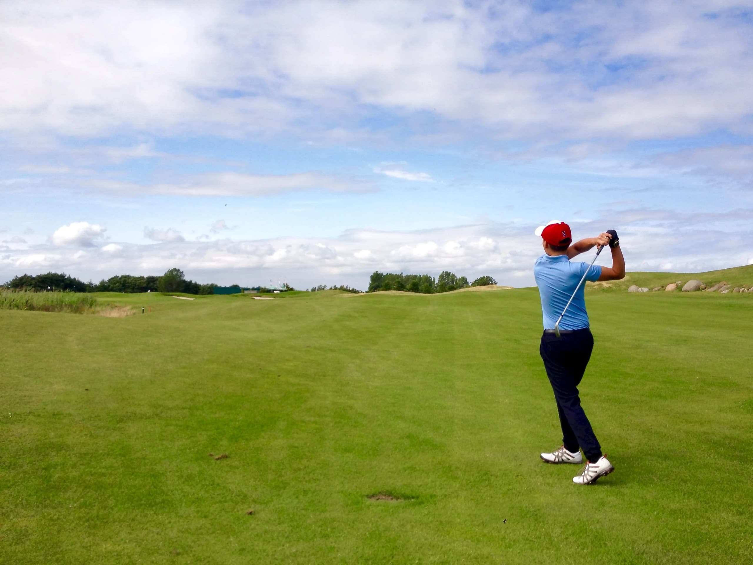 A golfer mid-swing on a sunlit links fairway under a wide summer sky